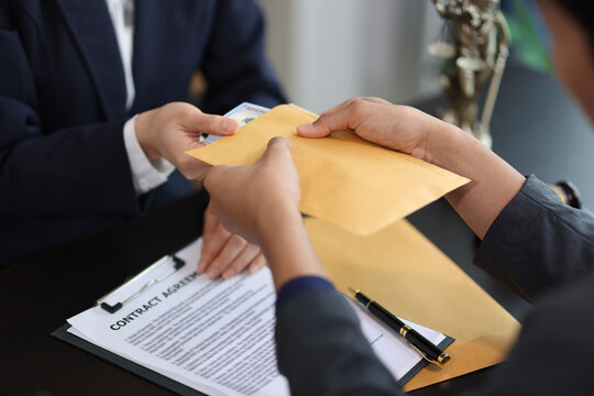 Businessman receiving bribe money in brown envelope from businesswoman at office.