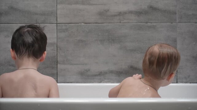 Two little boys having fun while taking bath in bathtub. Little children playing in the bath during the bathing.