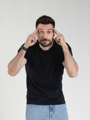 Caucasian 35 years old man in black T-shirt portraying deep disbelief with an ironic expression on his face and holding his fingers to his temples, emotional gesticulation.