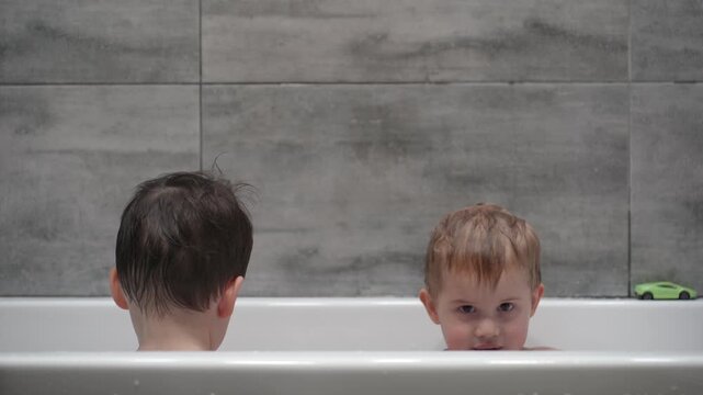 Two little boys having fun while taking bath in bathtub. Little children playing in the bath during the bathing.