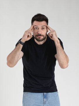 Caucasian 35 years old man in black T-shirt portraying deep disbelief with an ironic expression on his face and holding his fingers to his temples, emotional gesticulation.