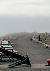 Fototapeta premium This image captures a foggy pathway leading into the distance with rustic wooden seating on either side, evoking a sense of tranquility and solitude by the water's edge.