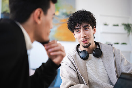 Two young men are engaged in a conversation, one with headphones around his neck, in a modern indoor setting.