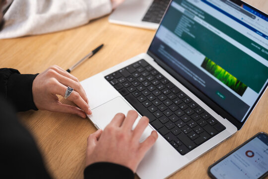 A person's hands are shown using a laptop and a smartphone on a wooden desk, indicating a focus on digital work or study.