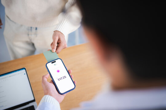 A person holds a smartphone displaying a payment amount of $17.25, ready to complete a transaction by holding a card near the device.