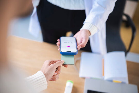 A person in a white coat holds a smartphone for a contactless payment as another person presents a card.