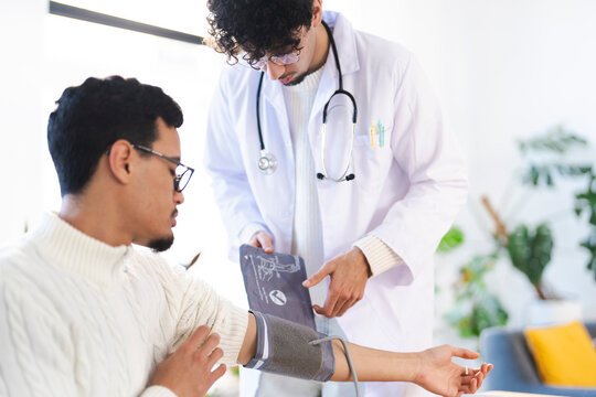 A doctor in a white coat takes a patient's blood pressure with a cuff and stethoscope in a bright, modern medical office.
