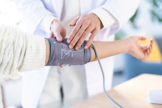 A medical professional in a white coat takes a patient's blood pressure with a cuff on their arm, focusing on health and wellness.