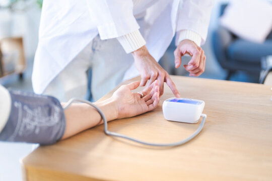 A medical professional in a white coat uses a digital device to check a patient's blood pressure, demonstrating a routine health check.