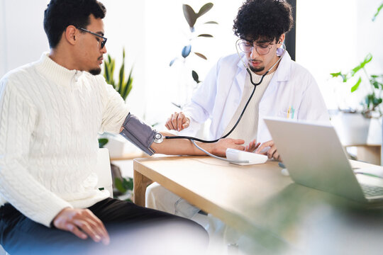 A doctor in a white coat uses a stethoscope and blood pressure monitor to check a patient's vital signs during a medical examination.