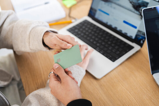 A person holds a payment card near a laptop, ready to make a transaction.
