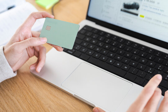 A person holds a payment card near a laptop, ready to make an online purchase.