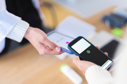 A person in a white coat holds a phone to scan a digital certificate on another phone, demonstrating a contactless verification process.
