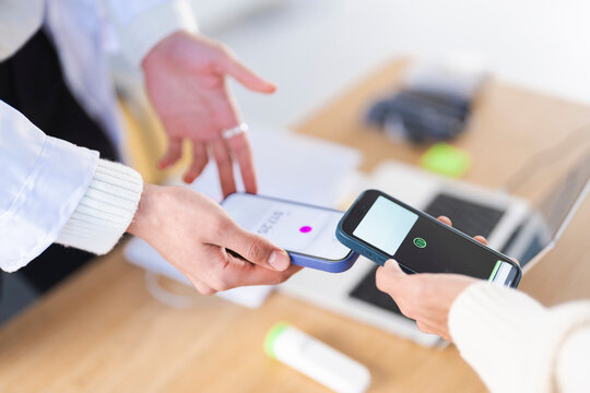 Two people are using their mobile phones to make a contactless payment. One phone displays a payment amount, while the other shows a payment confirmation screen.