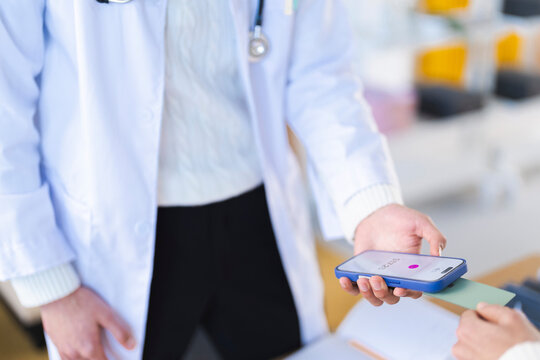 A medical professional in a white coat uses a smartphone to process a payment with a credit card, demonstrating modern healthcare transactions.