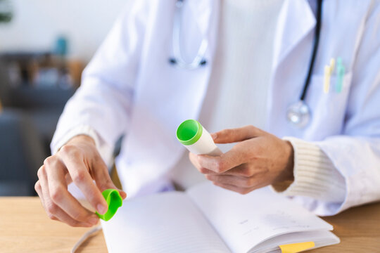 A medical professional in a white coat holds a small device and a green cap over an open notebook, suggesting a consultation or examination.