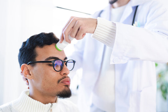A medical professional in a white coat uses a thermometer to check a patient's temperature on their forehead.