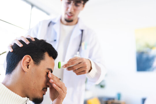 A doctor in a white coat takes a patient's temperature with a digital thermometer, showing care and concern for their well-being.