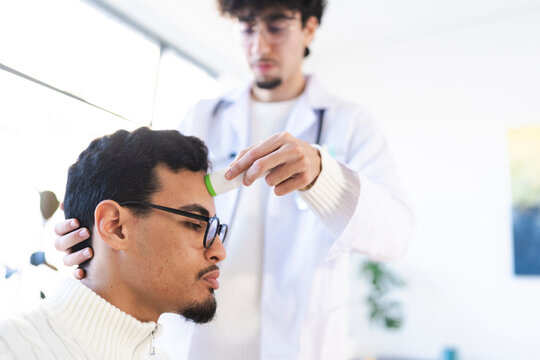 A medical professional in a white coat uses a non-contact thermometer to check a patient's temperature during a health screening.