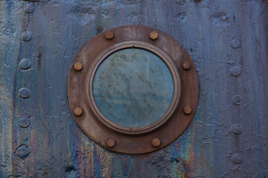 Close-up of a rusty porthole on an old metal ship hull.