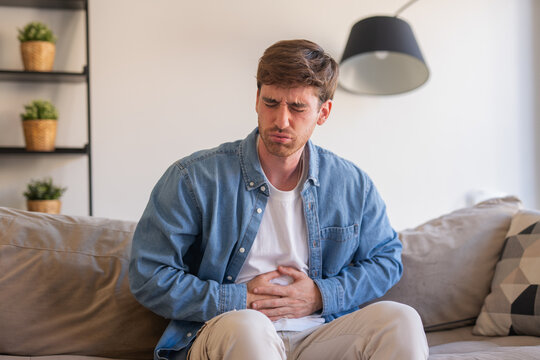 Sick young man in pain holding belly stomach feeling hurt abdomen ache gastritis pancreatitis symptoms or diarrhea, upset adult suffering from indigestion flatulence abdominal problem concept