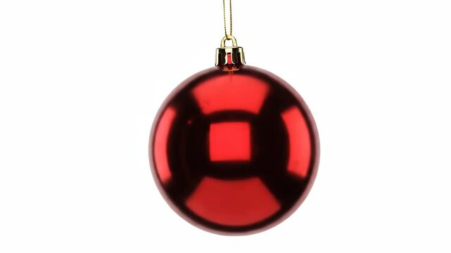 A red Christmas ornament hanging from a gold string on a white background