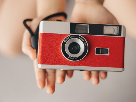 A child holds an old red film camera with a lens in his palms.