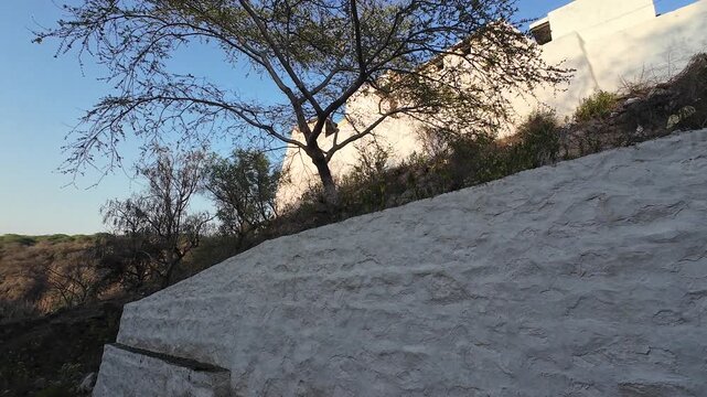 A historic white-painted main gate and stone pathway leading to a religious shrine situated on a rugged hill within the Aravalli Range in Nuh district