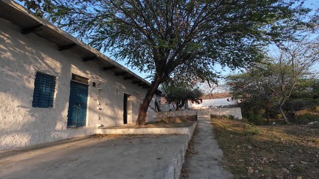 An ancient Hindu temple shrine situated on a rocky hill in the Aravalli range featuring traditional white-washed architecture and old twisted trees under a clear sky.