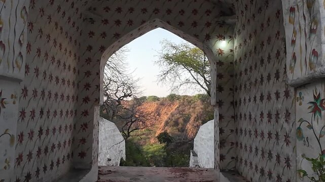 A historic white-painted main gate and stone pathway leading to a religious shrine situated on a rugged hill within the Aravalli Range in Nuh district