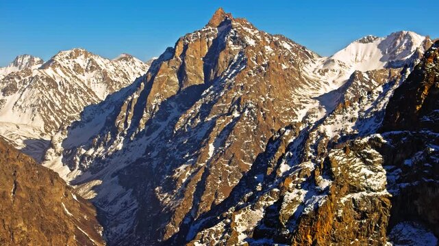 Majestic snow-covered mountains rise against a clear blue sky. drone view with parallax effect