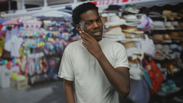 Young african american man in white polo wipes eye amid bustling street market stalls; sadness solitude longing.