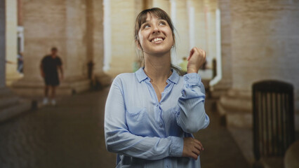 Obraz premium Woman smiling with arms crossed and pointing finger amid stone columns in a building; joy reflection.