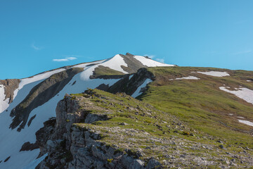 Scenic view above rocky ridge with cliff and snows against pointy peak. Alpine scenery with sharp rocks, sheer crags and peaked top. Tectonic plate protruding from an abyss. Stony pointed pinnacle. © Daniil