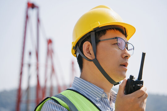 Engineer wearing yellow safety helmet holding walkie-talkie while directing operations on construction site