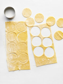 Fresh pasta dough is rolled out on a white surface with circular cutouts made for pasta shapes. This scene is ideal for food blogs, recipe websites, and cooking tutorials