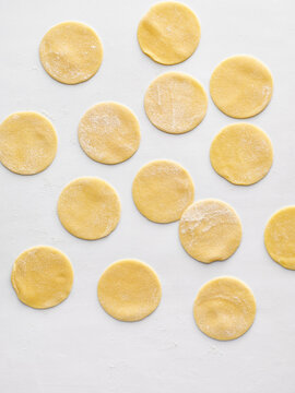 Round dough circles are arranged on a white surface, ready for filling to create ravioli. This composition is ideal for food blogs, restaurant menus, and culinary websites