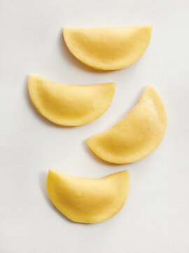 Four pieces of fresh pasta dough are arranged on a white background, showcasing the ravioli shape. This image is ideal for restaurant menus, cooking blogs, and culinary advertisements