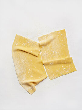 Freshly rolled pasta sheets dusted with flour on a white surface. Ideal for use in cooking blogs, restaurant menus, and culinary tutorials