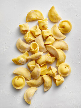 Various shapes of uncooked pasta are arranged neatly on a white surface. Perfect for restaurant menus, food blogs, cooking magazines, and social media posts