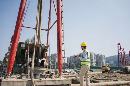 Construction worker inspecting drilling rig operation at a building site