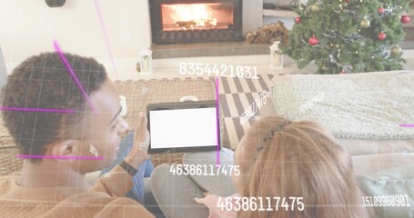 Naklejka premium Couple sitting closely on couch by fireplace in living room, holding tablet, viewing augmented grid