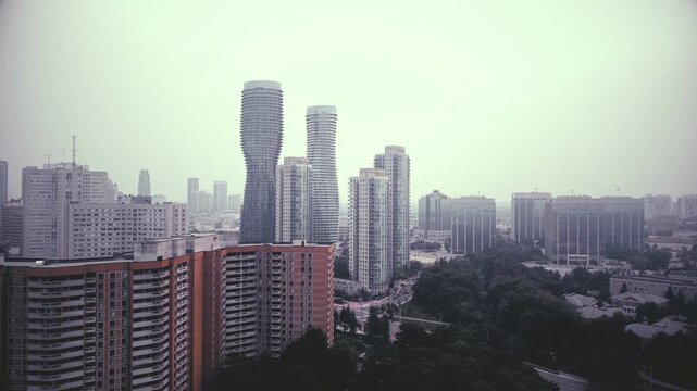 Aerial shot of the downtown city of Mississauga, Ontario, Canada skyline during a hazy late afternoon, with the sky filled with smoke from distant forest fires. Subtle blue tint color added.