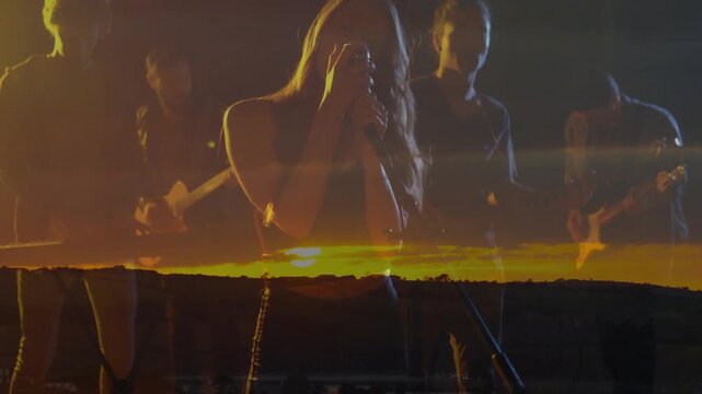 Cue urging lead singer moving center holding mic singing for focus band backing with sunset overlay