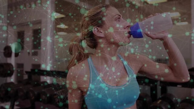 Woman lifting shaker and drinking in gym with dumbbell rack, green overlay tracking hydration