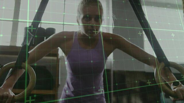 Female athlete gripping rings, leaning in gym and doing dips for strength while green grid shifting