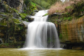 Fototapeta premium Silky waterfall in lush forest with mossy rocks and flowing stream, long exposure nature landscape