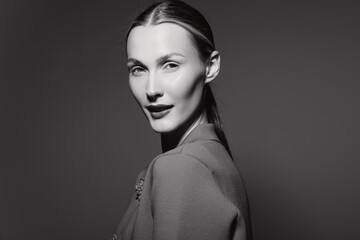 Fototapeta premium Portrait of a white woman with pale skin and sleek hairstyle wearing textured clothing on dark background. Concept of fashion, elegance, and monochrome beauty.