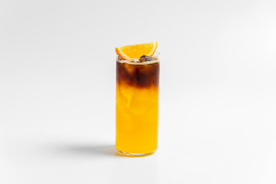 Refreshing bumble orange citrus juice and black coffee espresso drink with ice in a transparent collins highball glass on white background with copy space
