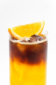 Refreshing bumble orange citrus juice and black coffee espresso drink with ice in a transparent collins highball glass on white background with copy space
